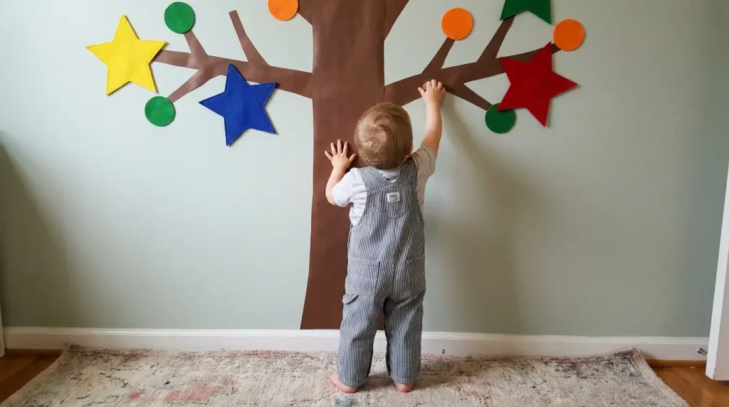 Toddler sticking big felt shapes on a contact paper tree